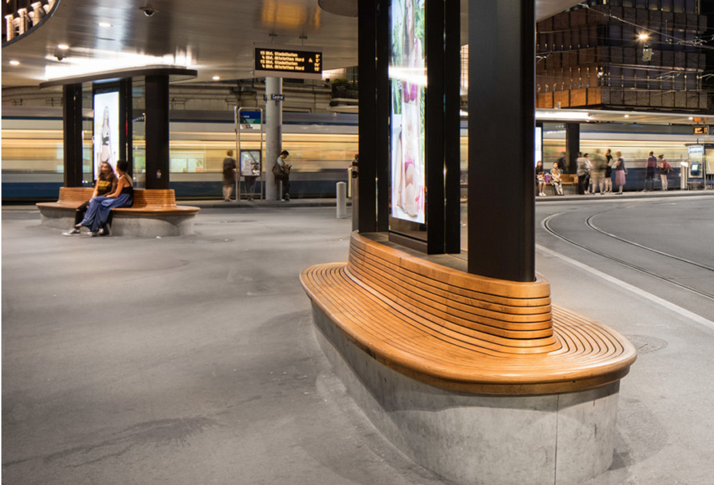 Runde Sitzbank aus Holz mit Lehne an einer Haltestelle des öffentlichen Verkehrs